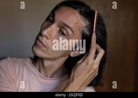 Junger Transgender-Mann (22) kämmt sich die Haare. Transgender-Konzept Stockfoto