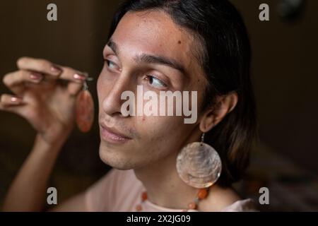 Der junge Transgender-Mann (22) ist in seinem Zimmer und zieht seine Accessoires an. Transgender-Konzept Stockfoto