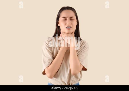 Junge Frau mit Halsschmerzen auf beigefarbenem Hintergrund Stockfoto