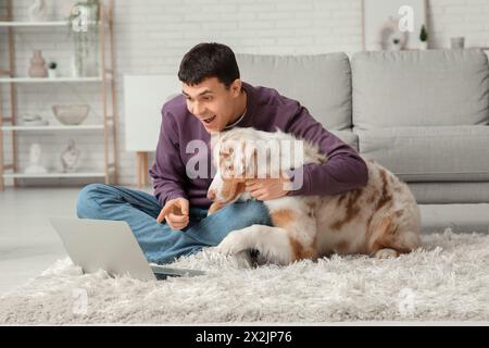 Junger Mann mit australischem Schäferhund und Laptop zu Hause Stockfoto