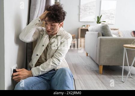 Ein junger Mann mit einem Verbrennungsgesicht, der zu Hause in die Steckdose gesteckt wird Stockfoto