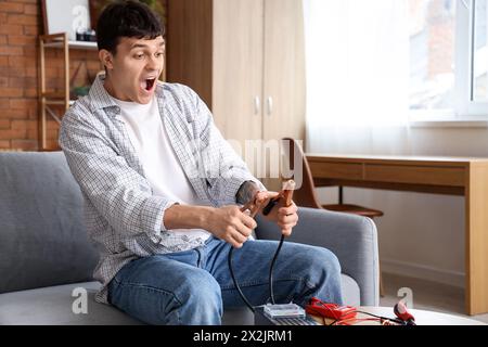 Ein junger Mann mit Stromschlag und Überbrückungskabeln zu Hause Stockfoto