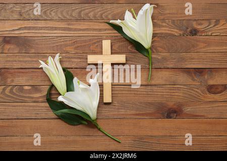 Weiße Lilien und Kreuz auf hölzernem Hintergrund Stockfoto