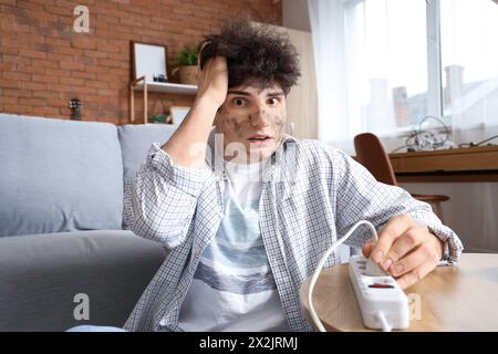 Ein junger Mann mit Verbrennungsgesicht, der zu Hause in das Verlängerungskabel gesteckt wird Stockfoto