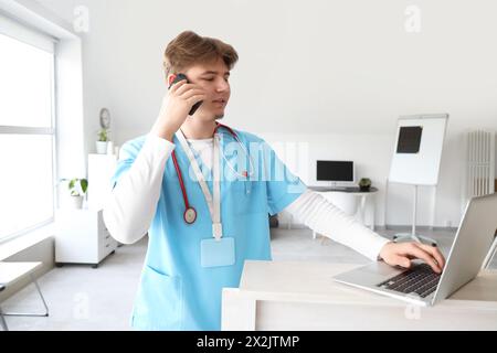 Männlicher Arztpraesident mit Laptop, der am Empfang in der Klinik per Handy spricht Stockfoto