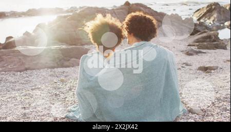Bild von Lichtflecken über zweirassigen Paaren, bedeckt mit Decken am Strand Stockfoto