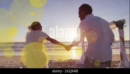 Bild von Lichtflecken über afroamerikanischen Paaren, die am Strand heiraten Stockfoto