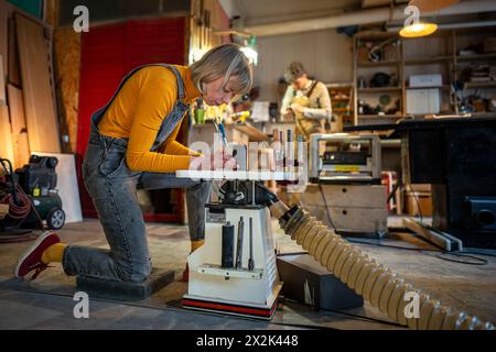 Eine fokussierte Zimmerfrau dreht Holzprodukte vorsichtig auf Drehwerken in der Familienschreinerei. Stockfoto