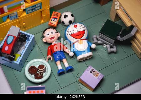 Japanische Spielzeugfiguren, namentlich Nobita und Doraemon, liegen zusammen auf dem Boden und lächeln zwischen den Gegenständen Stockfoto