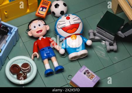 Japanische Spielzeugfiguren, namentlich Nobita und Doraemon, liegen zusammen auf dem Boden und lächeln zwischen den Gegenständen Stockfoto