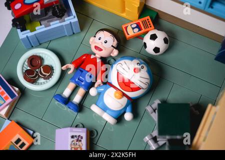 Japanische Spielzeugfiguren, namentlich Nobita und Doraemon, liegen zusammen auf dem Boden und lächeln zwischen den Gegenständen Stockfoto