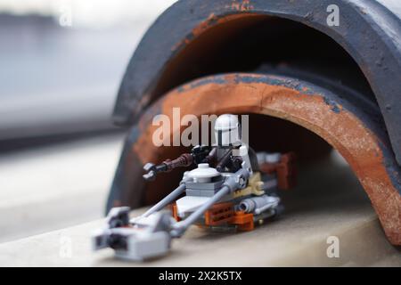 Die LEGO Minifiguren Mandalorian und Baby Yoda (Grogu) gehen durch einen dunklen Tunnel mit verschwommenem Hintergrund Stockfoto