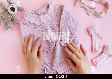 Rosafarbener Body mit Spielzeug gestricktem Hund, Socken und Stirnband. Set Babykleidung und Accessoires Sommer auf rosa Hintergrund. Fashion Neugeborene. Flach, oben Stockfoto