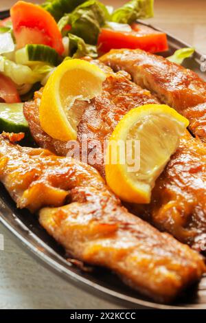 Geräucherte Makrelenfilets mit Salat und Zitrone auf einem schwarzen Teller. Auf einer Küchenarbeitsplatte bei spätabendlicher Sonneneinstrahlung Stockfoto