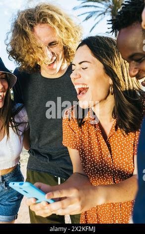 Multiethnische glückliche Millennial-Freunde, die während des Urlaubs im Freien ein Mobiltelefon benutzen Stockfoto