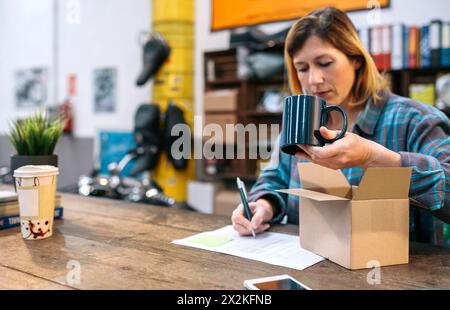 Blonde Unternehmerin, die neue Waren überprüft, die von einem Kurier erhalten wurden, um sie in ihrem lokalen Geschäft zu verkaufen Stockfoto