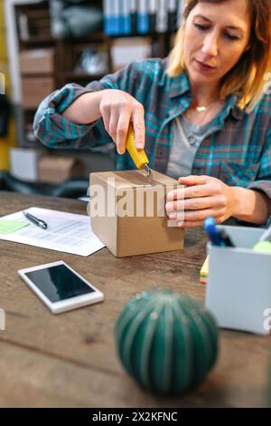 Junge Unternehmerin mit Schneidevorrichtung, die falsches Paket an Kunden im Online-Shop geschickt hat Stockfoto