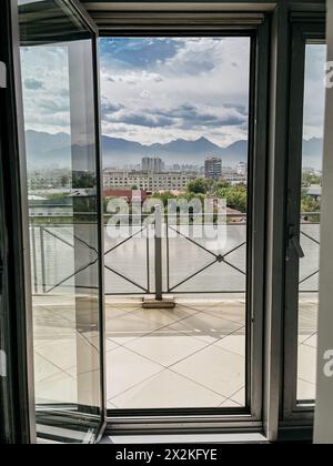 Ein atemberaubender Panoramablick auf die Skyline der Stadt und die schneebedeckten Berge, eingerahmt von einer offenen Tür, schaffen eine malerische Szene. Stockfoto