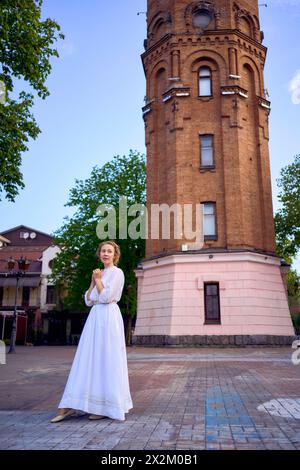 Eine schicke junge Frau in einem weißen Vintage-Kleid auf dem Platz in der Nähe des historischen Wasserturms in Vinnytsia Stockfoto