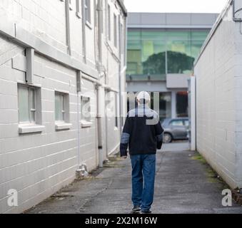 Mann, der zwischen den Mauern des Gebäudes zu dem auf der Straße geparkten Auto läuft. Stockfoto