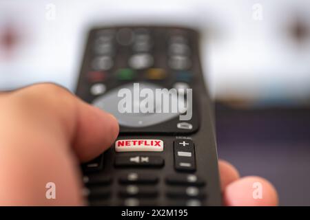 London. UK- 04.17.2024. Eine Hand, die eine Fernbedienung des Fernsehers hält, während der Finger die Netflix-Taste drückt. Stockfoto