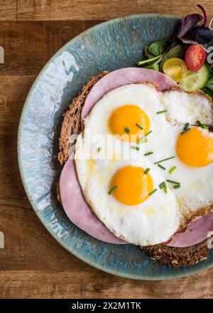 Blick von oben auf gebratene Eier und Schinken auf Brot auf einem Teller auf einem Holztisch im Café-Restaurant Stockfoto