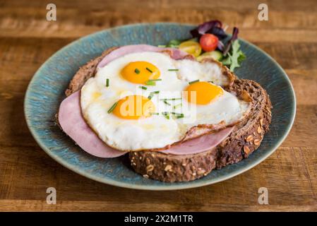 Spiegeleier und Schinken auf braunem Brot auf einem Teller auf einem Holztisch im Café-Restaurant Stockfoto