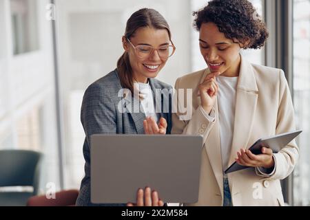 Stilvolle Managerinnen stehen im modernen Büro, während sie an einem Laptop oder einem digitalen Tablet arbeiten Stockfoto