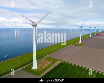 Ein faszinierender Blick auf eine Reihe eleganter, weißer Windräder in voller Bewegung, die im Frühling vor der lebhaften grünen Landschaft der Niederlande stehen. Windkraftanlagen auf See und an Land Stockfoto