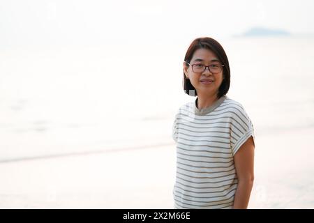 Porträt einer gesunden asiatischen Frau mittleren Alters in lässiger Weise am Strand stehend, helles Licht von hinten, Raum für Kopieren und Design. Stockfoto