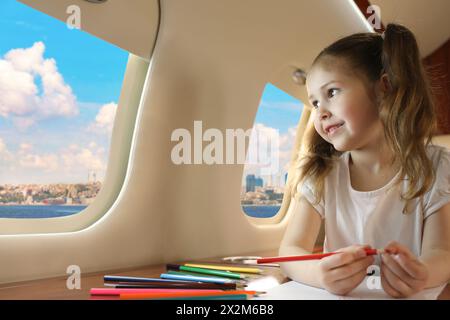 Niedliches kleines Mädchen, das während des Fluges aus dem Fenster auf den Tisch im Flugzeug schaut Stockfoto