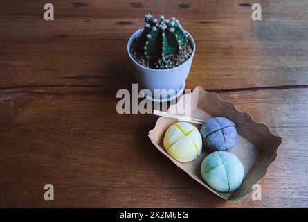 Japanisches Eis Mochi auf einem braunen Papierteller auf einem Holztisch mit natürlichem Licht aus dem Fenster, kleiner Kaktustopf in der Nähe des Mochi. Ansicht f Stockfoto