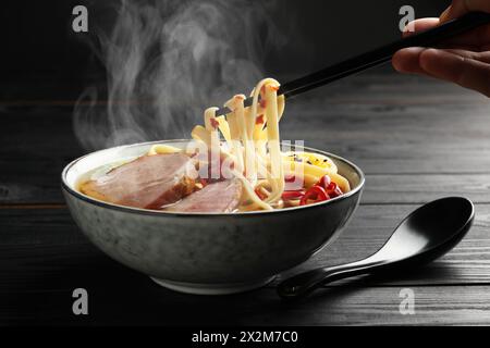 Frau isst heiße Ramen mit Stäbchen an schwarzem Holztisch, Nahaufnahme. Nudelsuppe Stockfoto