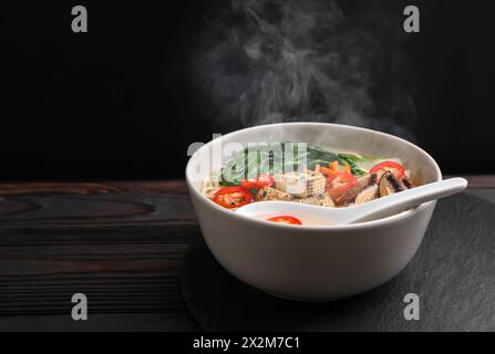 Schüssel mit heißen vegetarischen Ramen und Löffel auf dunklem Holztisch, Platz für Text Stockfoto