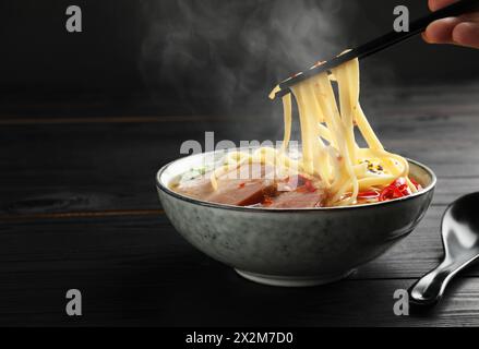 Frau isst heiße Ramen mit Stäbchen an schwarzem Holztisch, Nahaufnahme und Platz für Text. Nudelsuppe Stockfoto