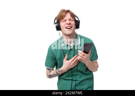 Moderner, stilvoller, energiegeladener junger rothaariger Mann in einem grünen T-Shirt hört Musik in den Kopfhörern Stockfoto