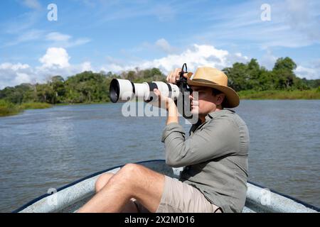 Mann mit Hut in einem Boot, der Fotos mit einer Kamera in einem Fluss macht Stockfoto