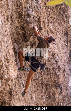 Ein fokussierter Kletterer mit Sicherheitsausrüstung klettert über eine anspruchsvolle felsige Klippe und zeigt Kraft und Wendigkeit Stockfoto