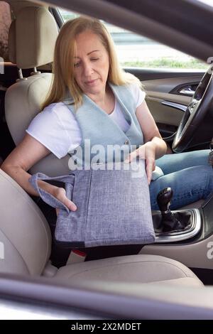 Eine Frau mittleren Alters hält aus Sicherheitsgründen eine Stofftasche auf dem Beifahrersitz eines Autos Stockfoto