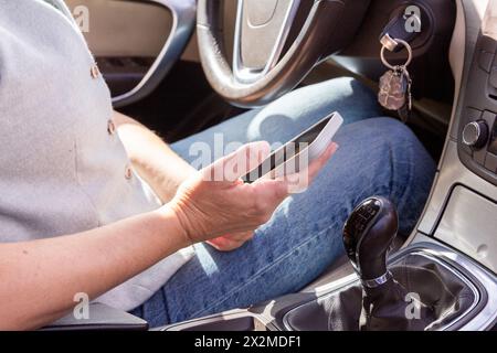 Nahaufnahme von Händen, die ein Smartphone in einem Fahrzeug halten, mit einem unscharfen Hintergrund des Fahrzeuginnenraums Stockfoto