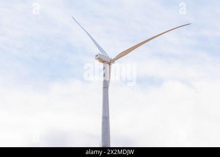 Eine einzige, elegante Windkraftanlage steht hoch vor dem Hintergrund von Wolken und symbolisiert nachhaltige Energie Stockfoto