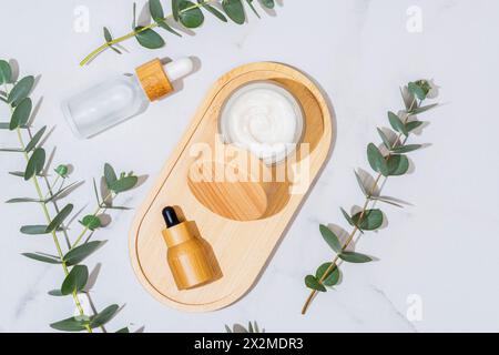 Eukalyptuszweige begleiten eine Holzpalette mit natürlichen Hautpflegeprodukten, die eine frische und organische Ästhetik emulieren Stockfoto