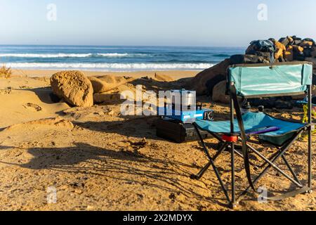 Eine ruhige Strandcampingszene mit einem tragbaren Herd und Stuhl am Sandstrand von Fuerteventura auf den Kanarischen Inseln, die einen idyllischen Urlaub bietet Stockfoto