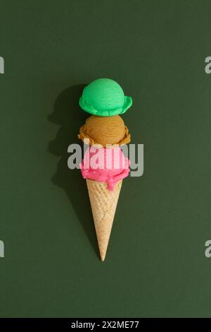 Dreilagige Eiskegel mit bunten Schaufeln auf grünem Hintergrund Stockfoto