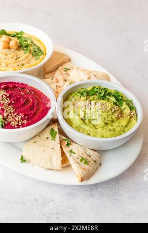 Verschiedene Hummussorten, darunter Klassik, Rüben und Avocado, serviert mit Pitabrot auf einem weißen Teller. Stockfoto