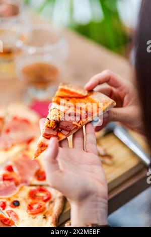 Eine nicht erkennbare Person, die nicht zu erkennen ist, isst ein frisch gebackenes Stück hausgemachte Pizza, garniert mit Tomatensauce, herzhaftem Fleisch und geschmolzenem Käse. Stockfoto