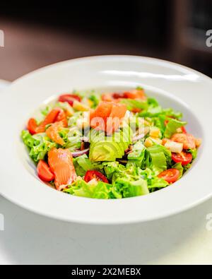 Ein lebhafter Haussalat mit frischem Mezclum, saftigen Lachsscheiben, Reifen Kirschtomaten, knusprigen Zwiebeln, saftigem Apfel, und cremige Avocado serviert in A Stockfoto