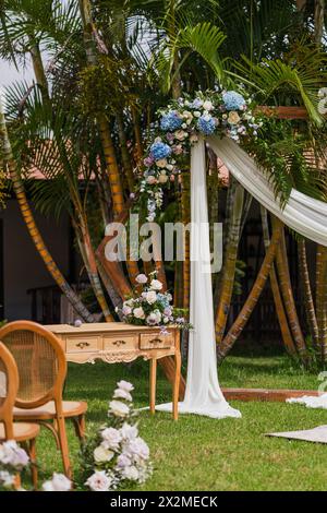 Ein elegant dekorierter Hochzeitsbogen, der mit einer wunderschönen Auswahl an Blumen geschmückt ist, steht in einem tropischen Garten und schafft eine perfekte Kulisse für roma Stockfoto