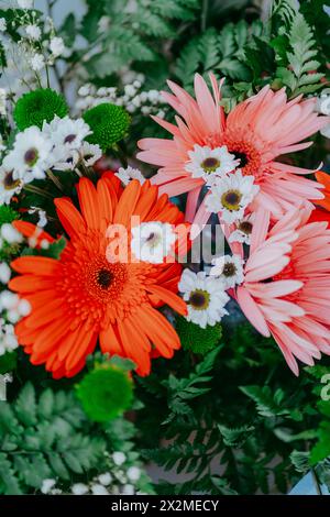 Ein Brautstrauß aus nächster Nähe mit leuchtenden orangen Gerberas, rosafarbenen Gänseblümchen und grünem Laub, perfekt für Hochzeiten Stockfoto