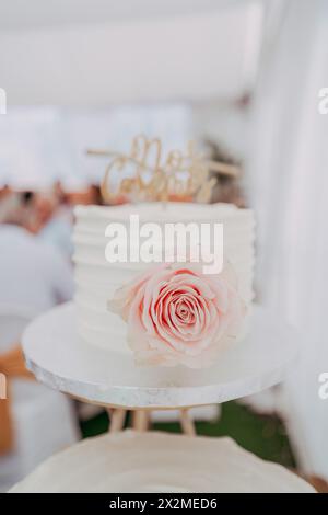 Eine exquisite Hochzeitstorte mit strukturiertem Zuckerguss und einer zarten rosa Rose, die anmutig darauf platziert ist, verkörpert Eleganz und Einfachheit Stockfoto